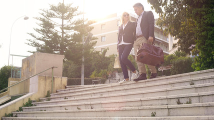 Happy couple with bags leaving hotel and going downstairs, vacation travel