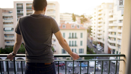 Male standing on balcony and enjoying view on street after hard working day