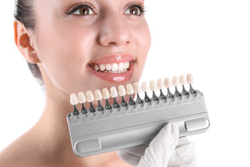 Dentist checking young woman's teeth color on white background, closeup