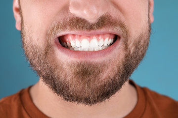 Young man with healthy teeth smiling on color background, closeup