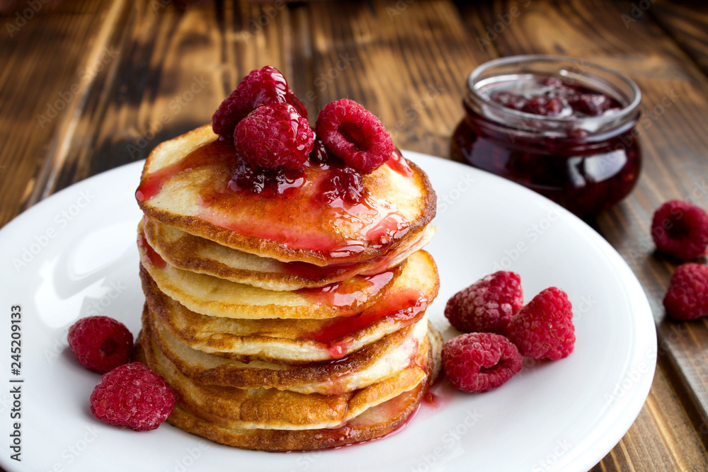 Wall mural Homemade pancakes with raspberry jam in the white plate on the brown wooden background