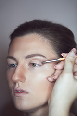 Young beautiful woman applying make-up by make-up artist. Process of making makeup.