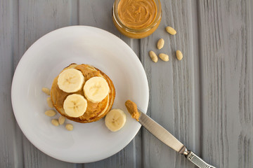 Homemade pancakes with peanut paste and banana in the white plate on the grey wooden background.Top view.Copy space.