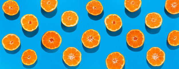 Mandarin halves in lines with hard shadows on blue background, flat lay image.