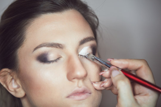 Young beautiful woman applying make-up by make-up artist. Process of making makeup.