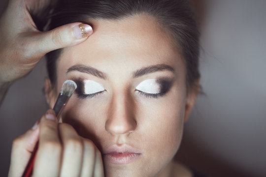 Young beautiful woman applying make-up by make-up artist. Process of making makeup.