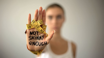 Not skinny enough written on woman palm with tape, severe diet, anorexia - obrazy, fototapety, plakaty