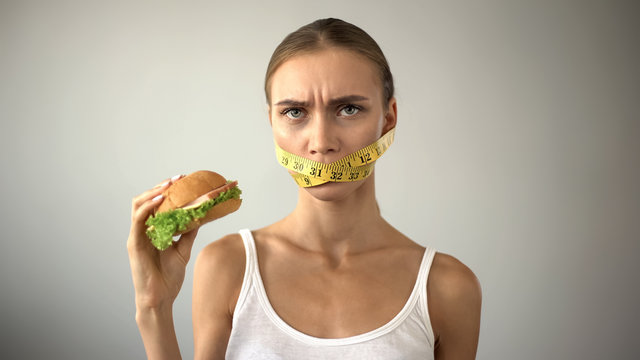 Slim girl with taped mouth fights with temptation to eat burger, dieting