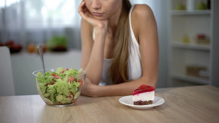 Underweight girl choosing between cake and salad, healthy vs high-calorie food