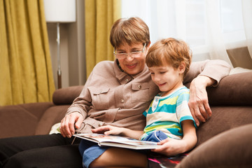Grandmother with child grandson  having a great time  and looking old family photo album at home. 