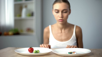 Obraz na płótnie Canvas Anorexic girl choosing weight loss drugs instead of vegetables, unhealthy diet