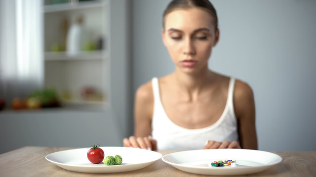 Anorexic girl choosing weight loss drugs instead of vegetables, unhealthy diet
