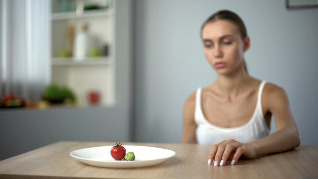 Exhausted slim woman looking at small portion of breakfast, self-destruction - Powered by Adobe