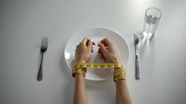 Hands tied with tapeline on empty plate, girl obsessed with counting calories