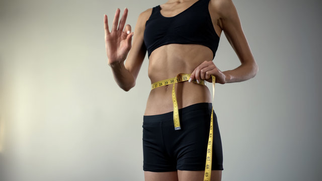 Slim girl measuring waist with tape-line, showing ok, anorexia as mental illness