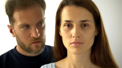 Pensive woman looking at camera man behind wife, inability to make own decisions