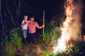 Obraz premium father and son, villagers burning brushwood on fire at night, seasonal cleaning of the countryside area, village lifestyle