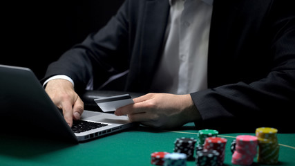 Male entering card number on laptop application, chips on table, online gambling