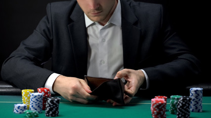 Upset gambler looking in empty wallet, loser at casino table, game addiction