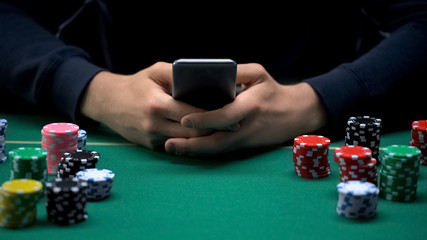 Male player betting on smartphone application, casino chips table, online game