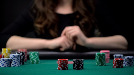 Female player waiting for others bets at casino poker table, gambling addiction