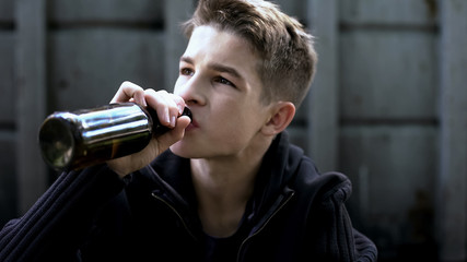 Boy drinking beer sitting in backstreet, desire to be older, first experience