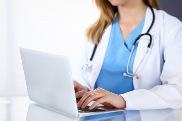 Doctor typing on laptop computer while sitting at the glass desk in hospital office. Physician at work. Medicine and healthcare concept