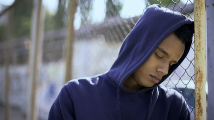 Upset boy leaning on fence, migrant child separated from family and detained