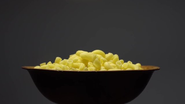 Raw macaroni in rotation. Elbow macaroni. Macaroni rigati close up.  Raw pasta  grey background. Italian cuisine concept.