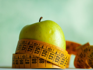 Obesity concept. A green apple and a tape measure on top of a table