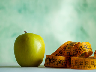 Obesity concept. A green apple and a tape measure on top of a table