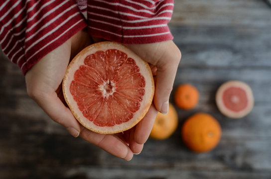 Hands of a young woman holding a red grapefruit. Healthy food concept, top view.