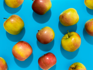 Apples with hard shadow on blue background, flat lay image.