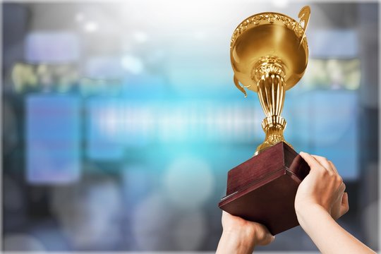 Close-up human hand holding golden Trophy on blurred  background