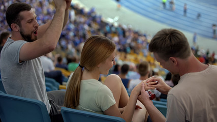 Man proposing marriage to girl at stadium, wearing engagement ring, romantic