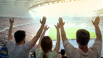 Young football fans with raised hands supporting national team during match