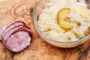 Traditional organic raw and fermented sauerkraut with pickled Persian cucumbers and homemade smoked pork sausage on olive wood cutting board.