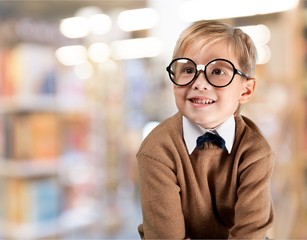 Cute little schoolgirl in glasses on library background