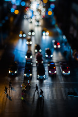 Night traffic in Bangkok. People cross the street at a pedestrian crossing. Car headlights are out of focus in the background. Night city lights up. Car headlights are reflected from the asphalt road 