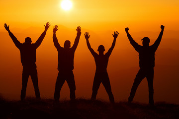 Silhouette group of hikers greetings sun with raised hands against sunset. Hikers walking on a mountain at sunset.