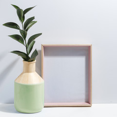 Mock up white frame and branch with green leaves in ligth-green vase on book shelf or desk. Minimalistic concept.