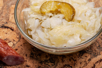Traditional organic raw and fermented sauerkraut with pickled Persian cucumbers and grass fed beef smoked sausage stick on olive wood cutting board.