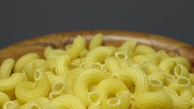 Raw macaroni in rotation. Elbow macaroni. Macaroni rigati close up.  Raw pasta  grey background. Italian cuisine concept.