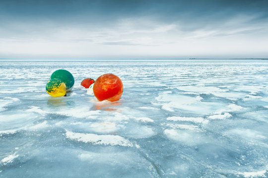 Colorful buoys in frozen lake against sky