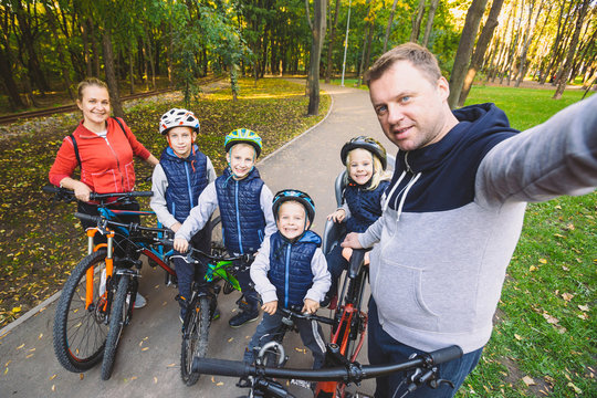 The theme family sports outdoor recreation. large family Caucasian 6 people mom dad and 4 children three brothers and sister ride bicycles in park on bicycle path. Father holds camera makes photo