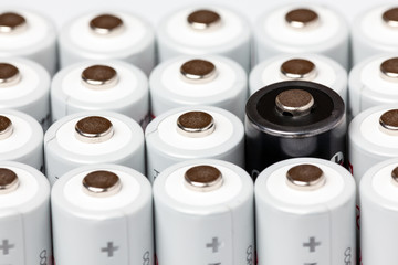 AA batteries are located close to each other. Close-up of all white batteries, except one black, on a white background. Battery technology