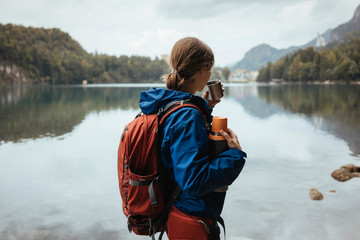Side view of female hiker drinking coffee and looking at lake in forest