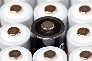 AA batteries are located close to each other. Close-up of all white batteries, except one black, on a white background. Battery technology