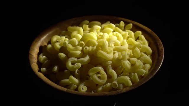Raw macaroni in rotation. Elbow macaroni. Macaroni rigati close up.  Raw pasta  black background. Italian cuisine concept.