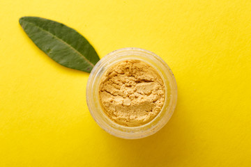  flat lay a jar eye shadow yellow summer color on a colored background with green leaves